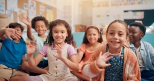 Waving, happy and portrait of children in classroom for language development, learning or growth. Smile, kids and cute students greeting for morning lesson with education at elementary school.