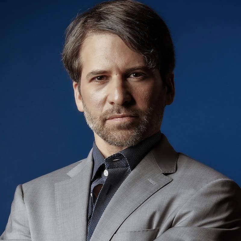 Man in a gray suit with a blue background, representing professionalism and expertise in education and tutoring services.